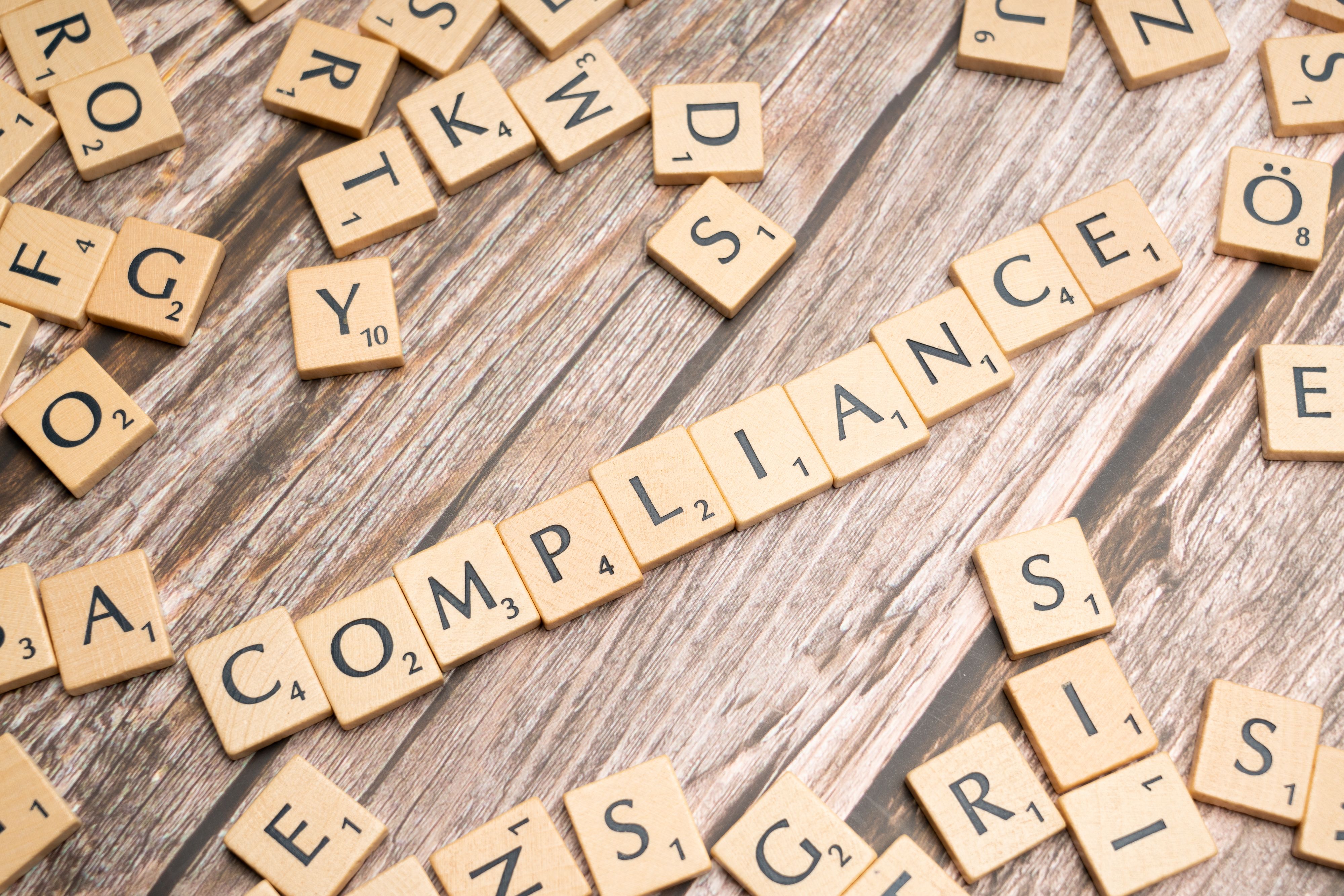 Wooden letter tiles spelling COMPLIANCE, representing legal sector regulation