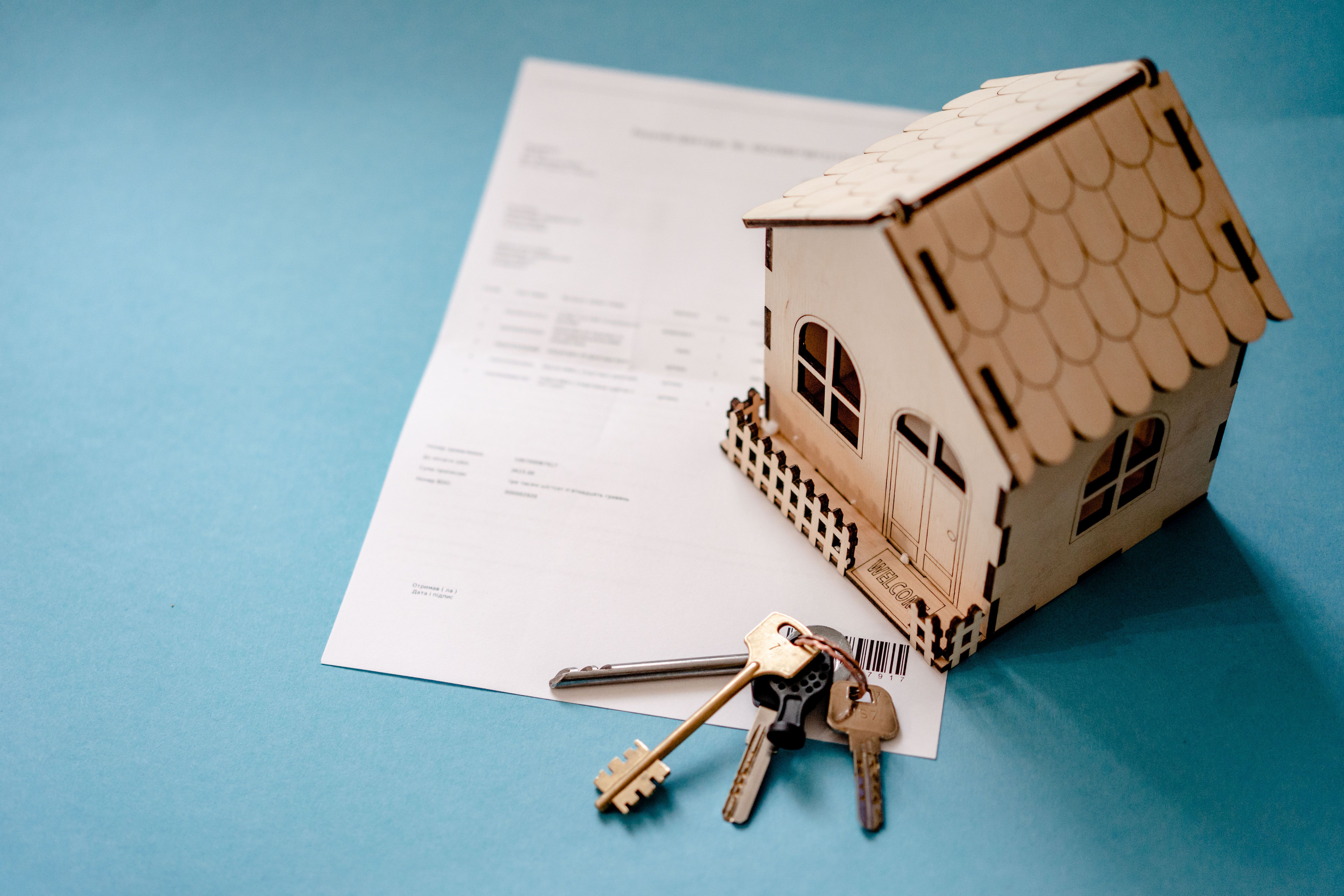 Miniature wooden house with keys and a contract symbolizing real estate transactions