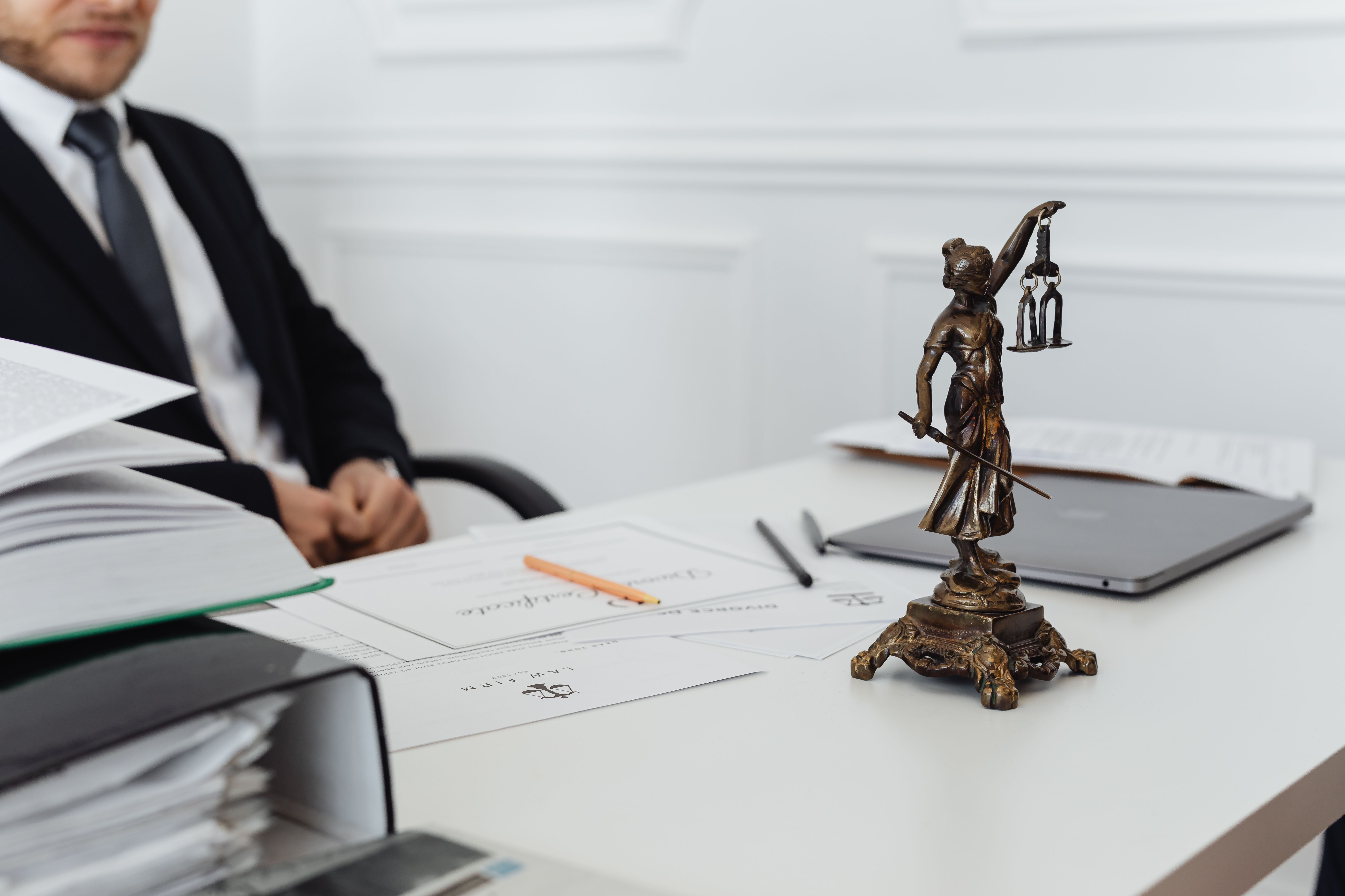 Legal professional's workspace with Lady Justice statue, documents and a laptop